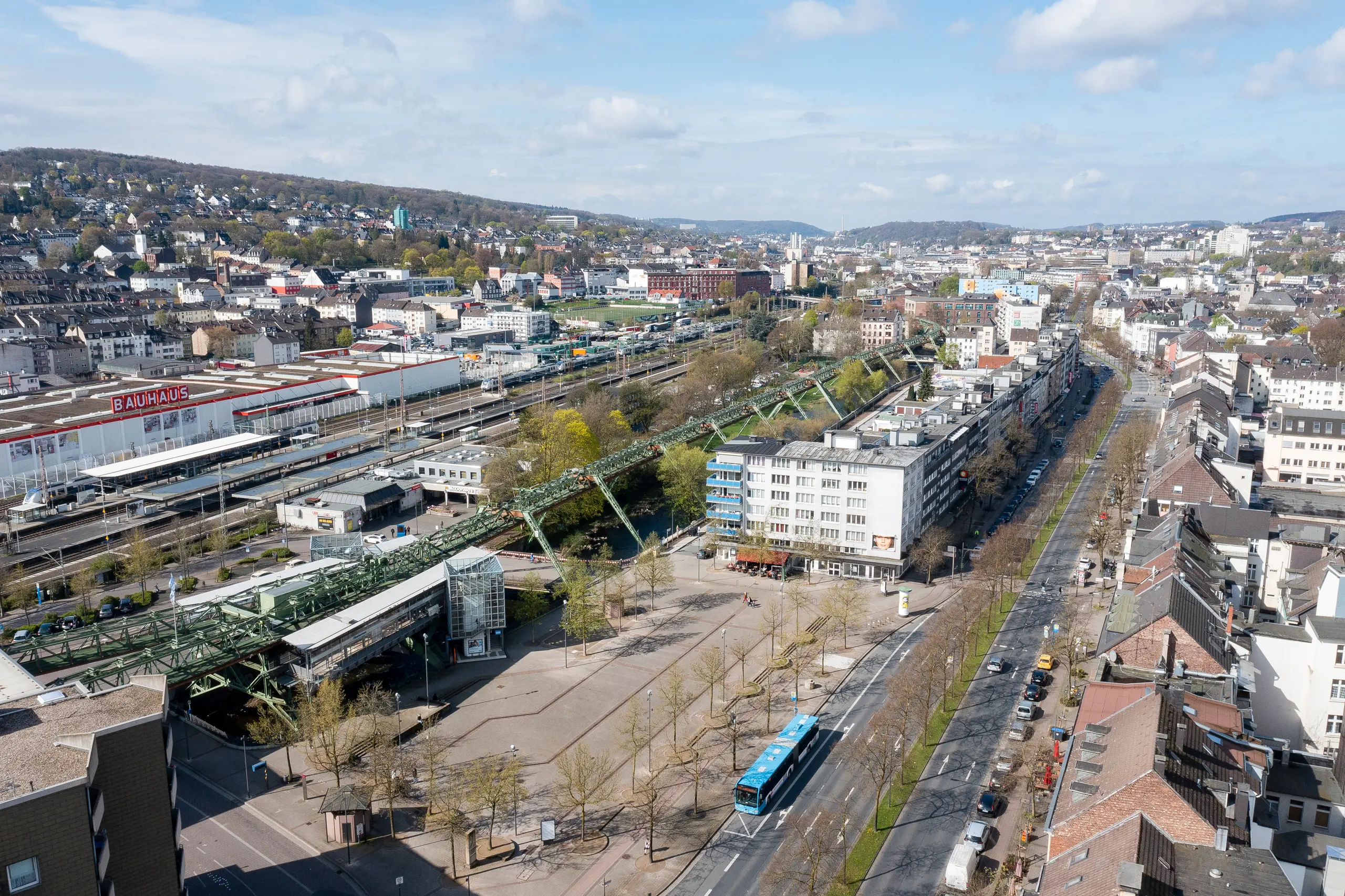 Luftaufnahme von Wuppertal im Jahr 2025 mit der Schwebebahn, einer Hauptverkehrsstraße und umliegenden Gebäuden.