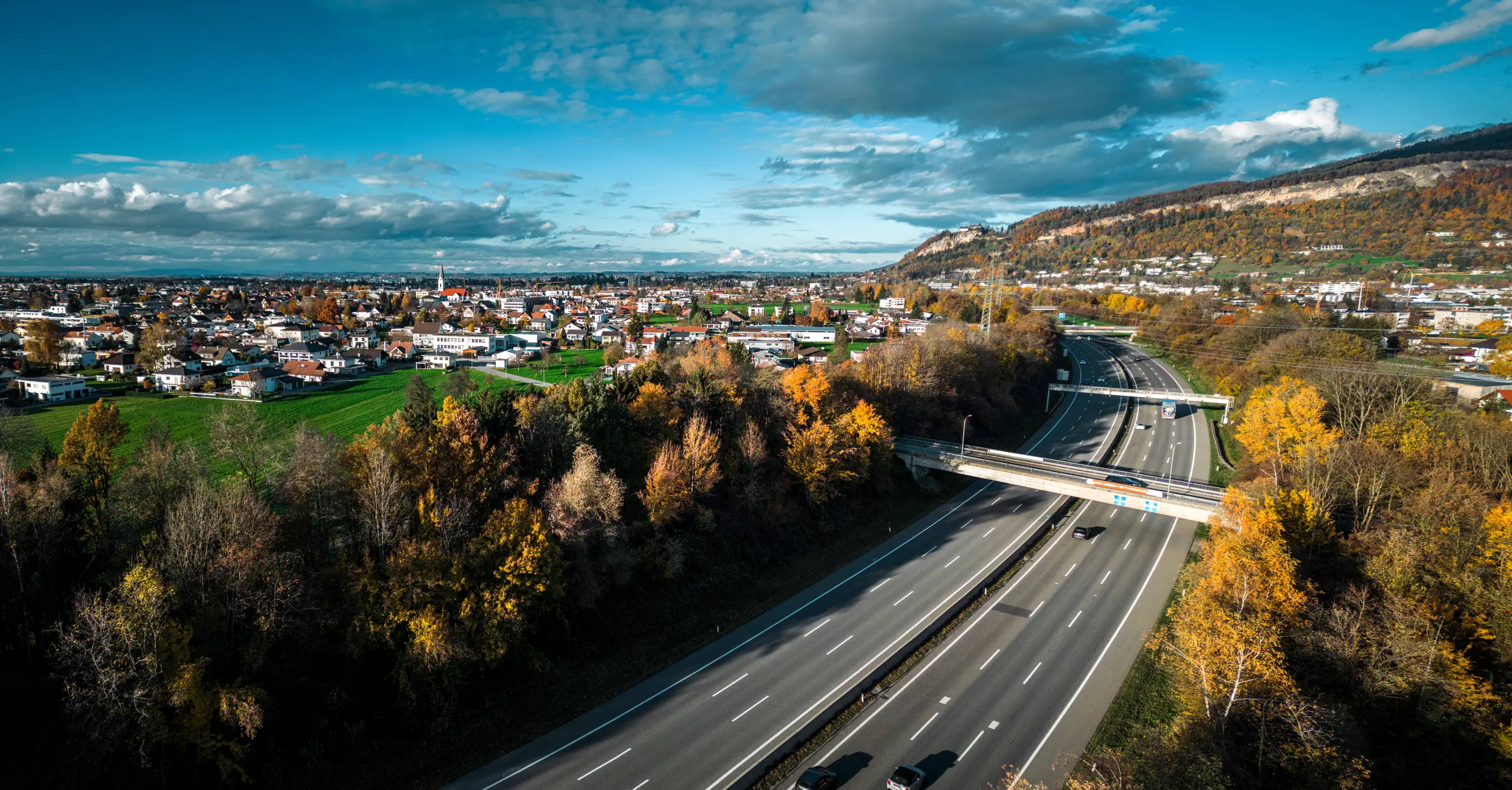 Luftaufnahme der Autobahn bei Bregenz, Österreich, umgeben von Herbstlandschaft und urbanen Strukturen. Der Verkehr fließt über breite Fahrbahnen.