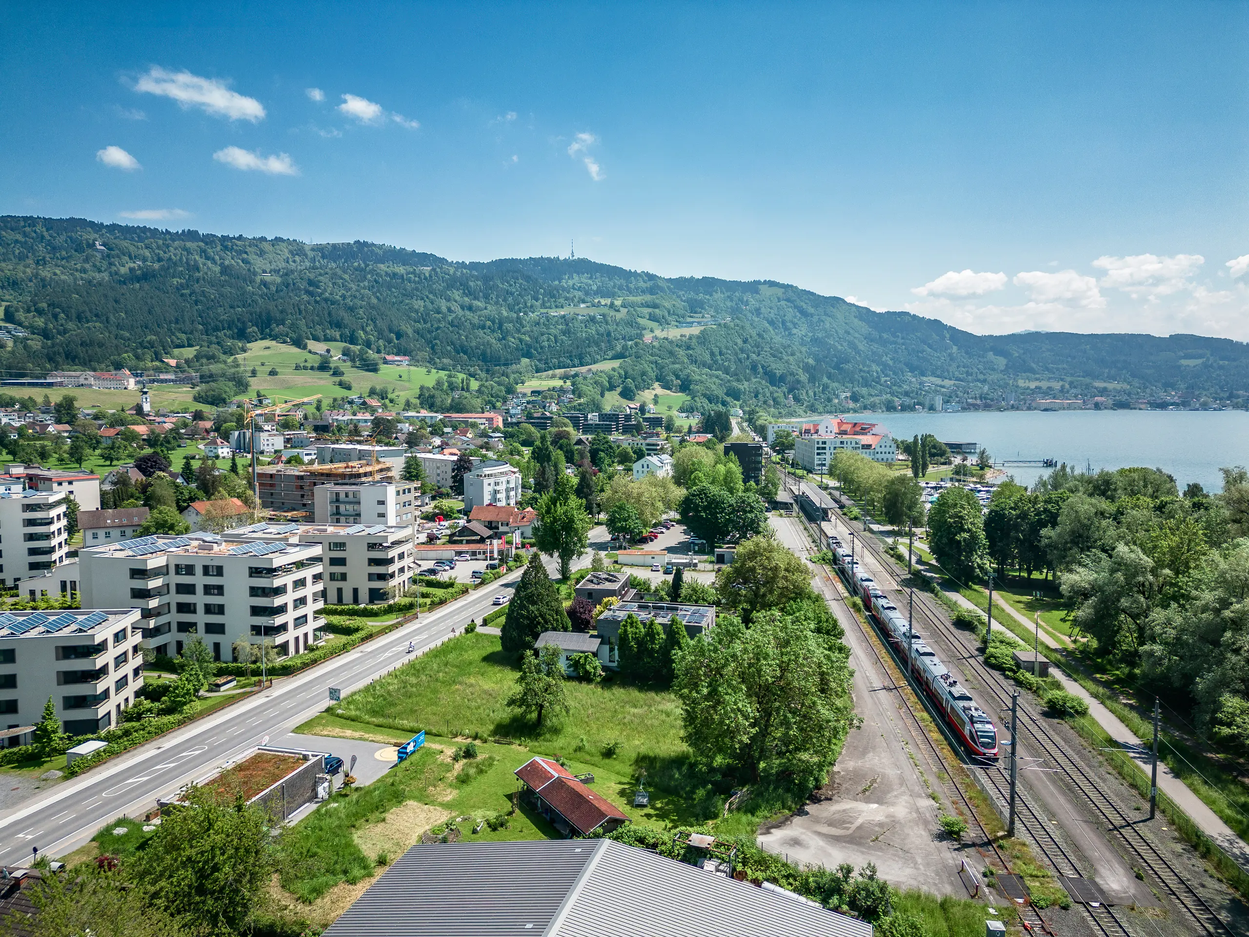 Luftaufnahme von Lochau, Österreich, mit Blick auf den Bodensee, Wohngebäude und eine Bahnstrecke in der heutigen Zeit.