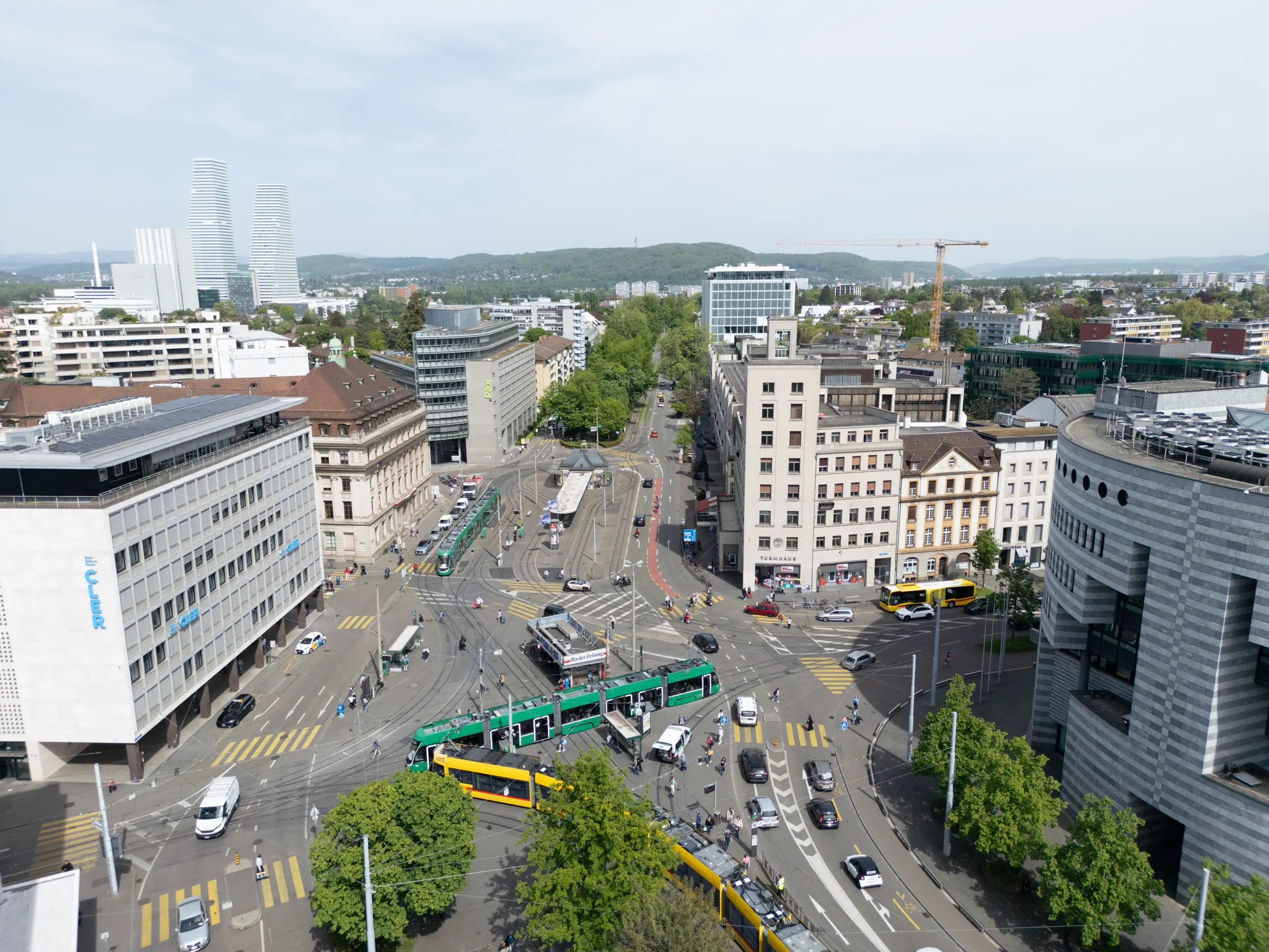 Luftaufnahme des Aeschenplatzes in Basel im Jahr 2025 mit dichtem Verkehr, Straßenbahnen und wenig Grünflächen.