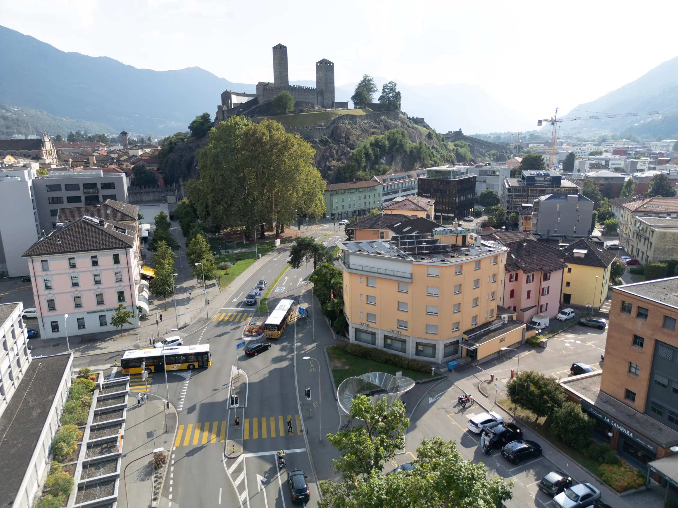 Luftaufnahme von Tessin, Schweiz, mit Straßenverkehr und urbaner Infrastruktur, umgeben von Bergen und historischen Gebäuden.