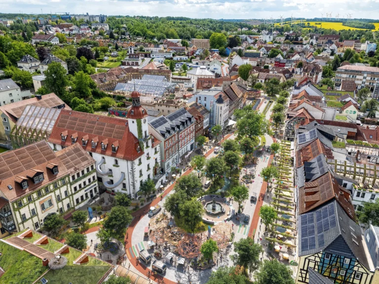 Zukunftsvision des Marktplatzes in Schmölln 2045 – grüne, autofreie Innenstadt mit begrünten Gebäuden, urbanen Gärten, erneuerbaren Energien und neuen Aufenthaltsbereichen.